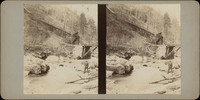 Unidentified man standing near a creek with a mining chute in the background